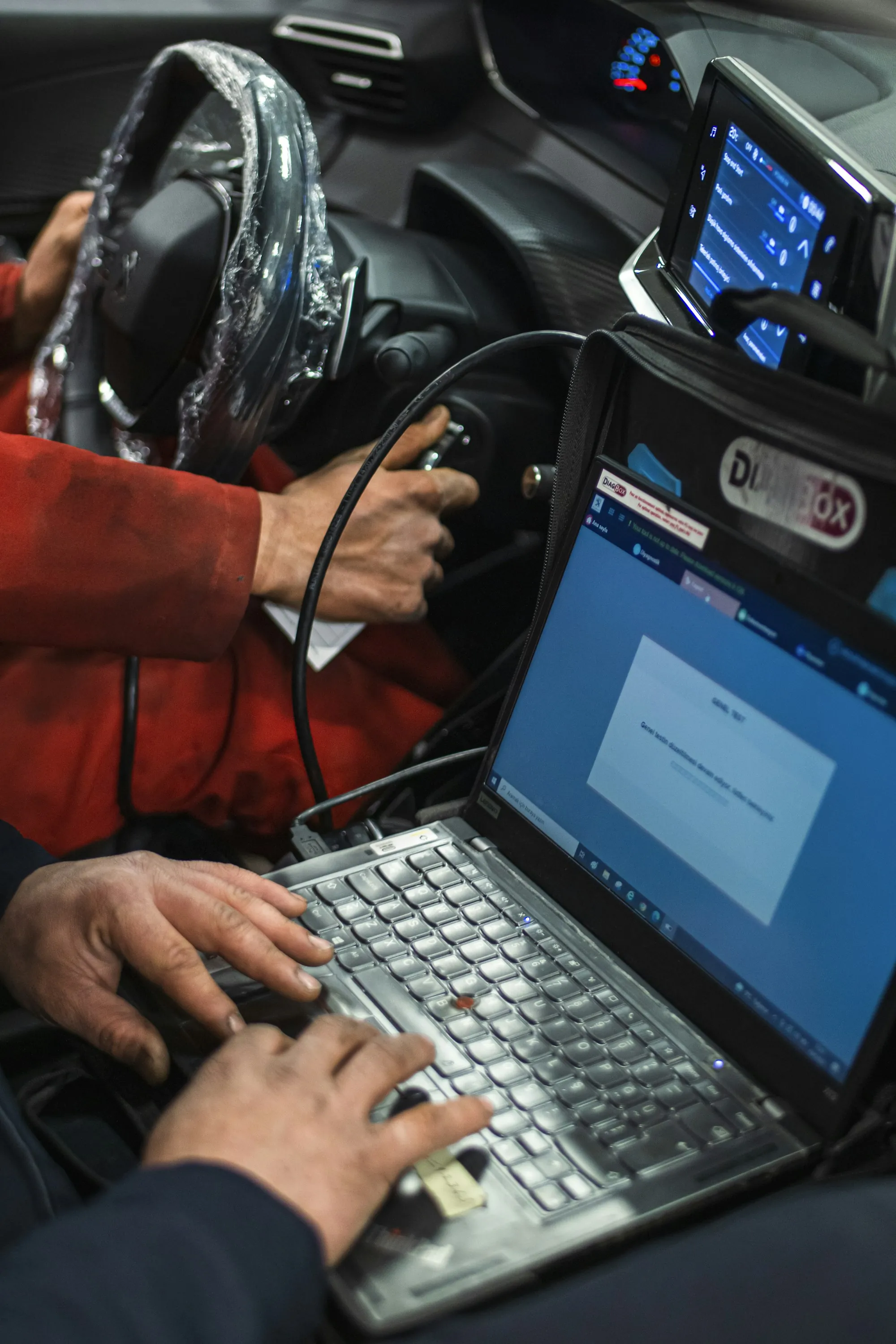 Mechanic typing on a laptop connected to a car