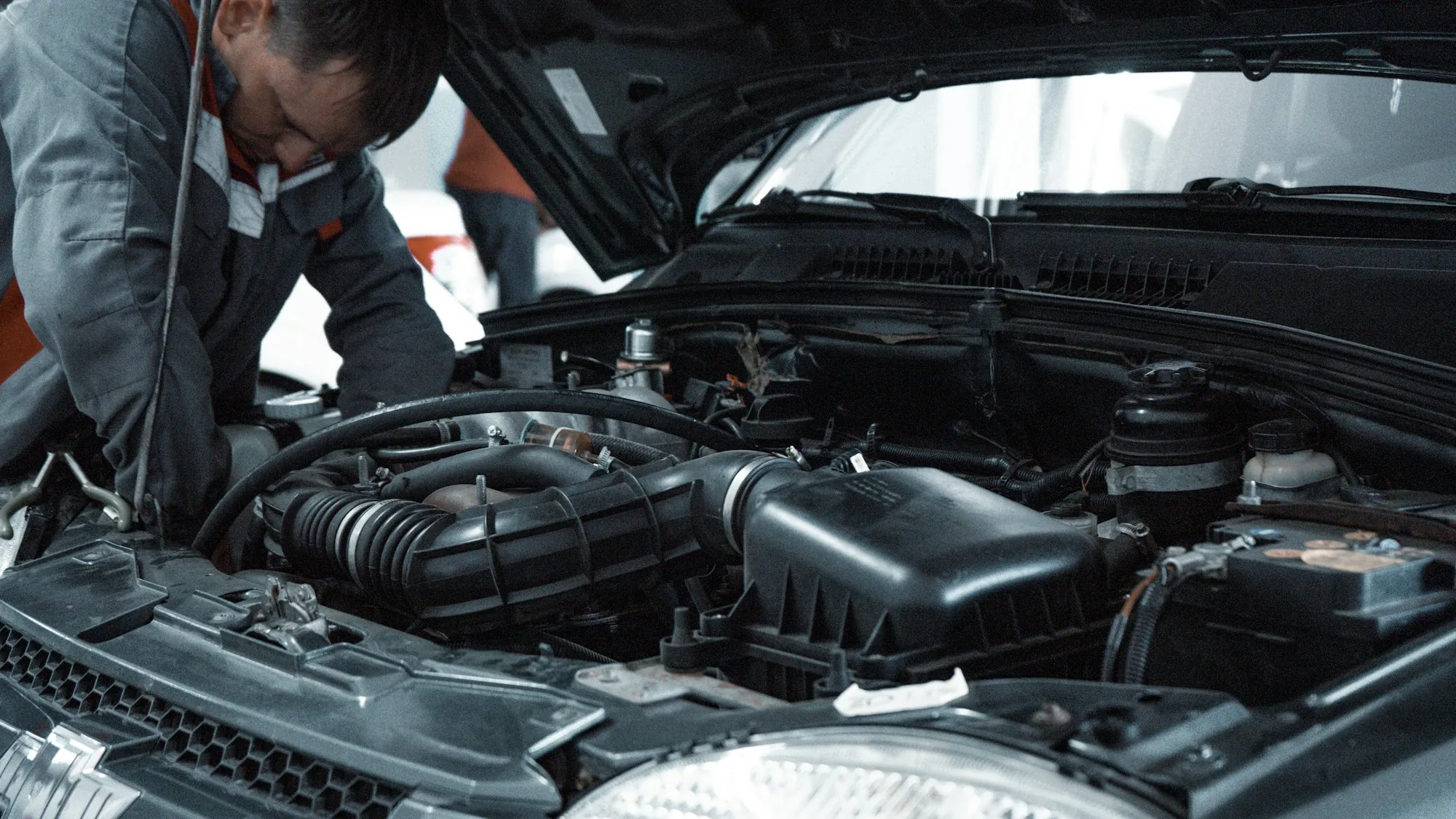 Two mechanics working under the hood of a vehicle