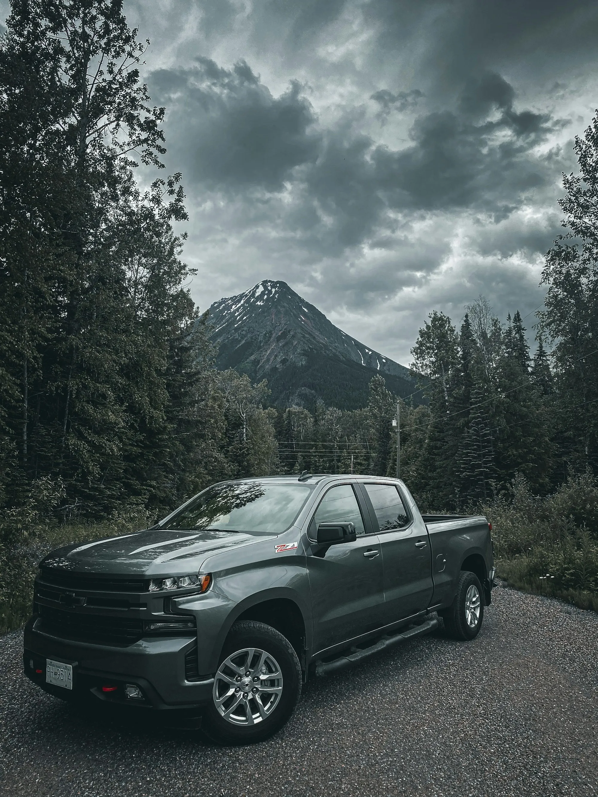 Dark pickup on a forest road under cloudy mountain peaks