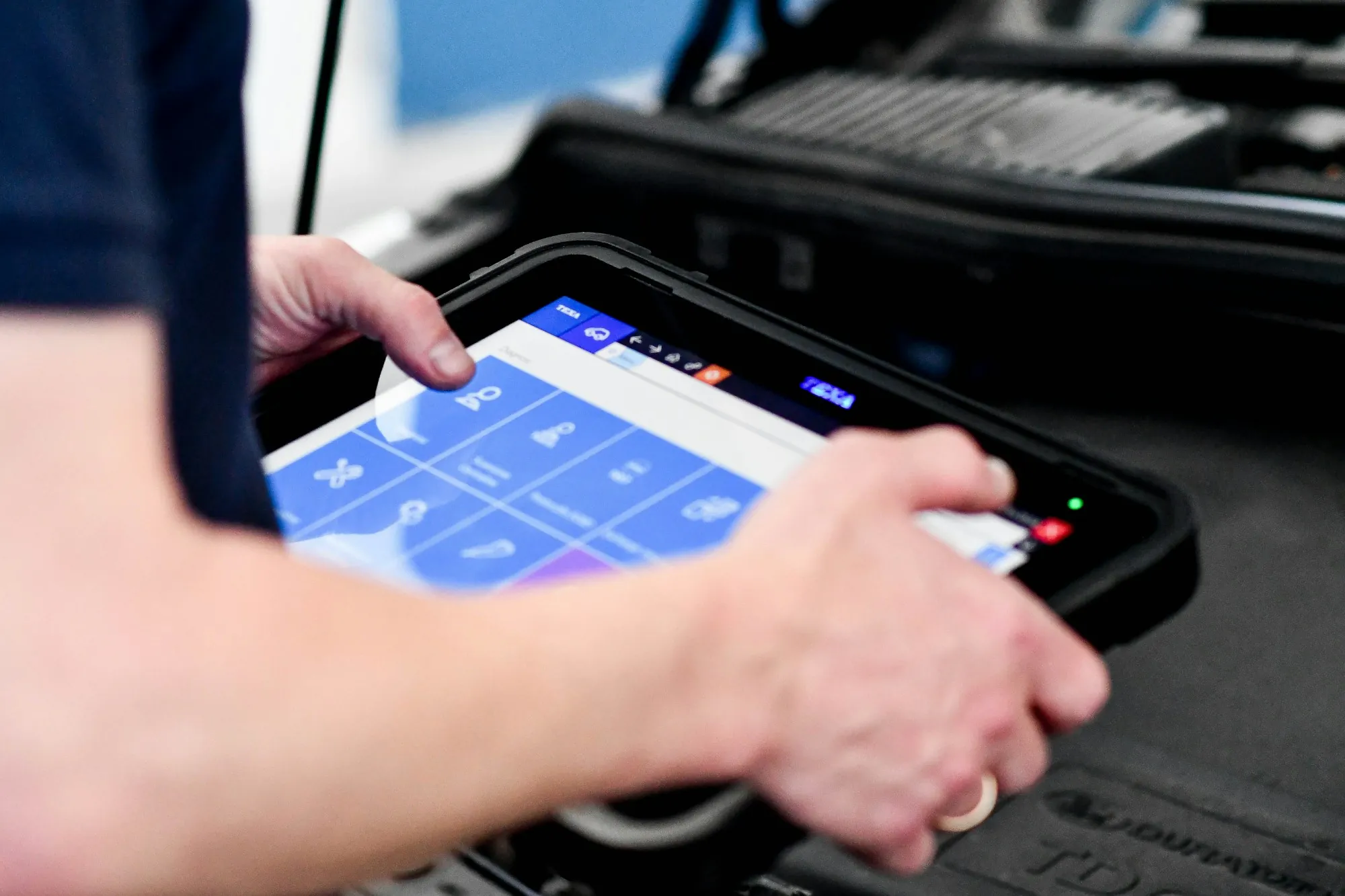Hands holding a diagnostic tablet near an open engine bay