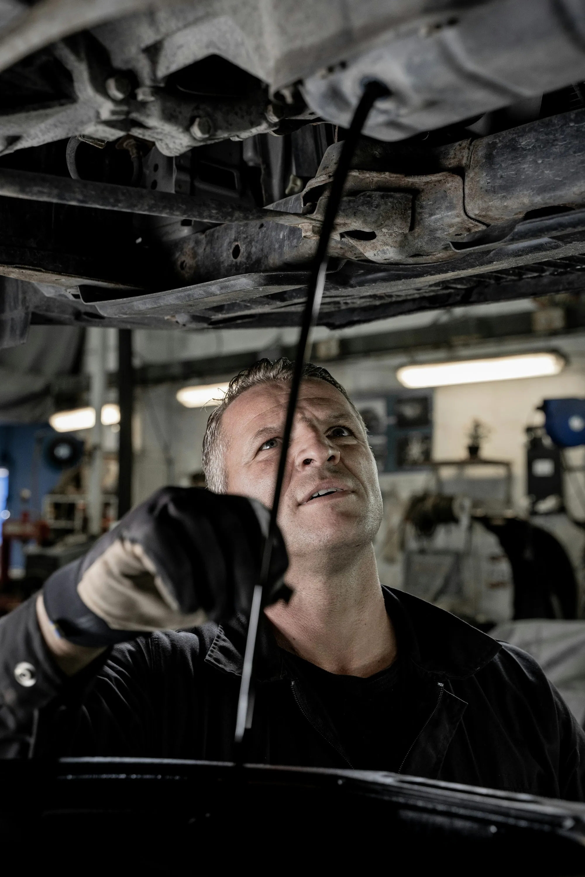 Technician tightening a fitting on a lifted vehicle